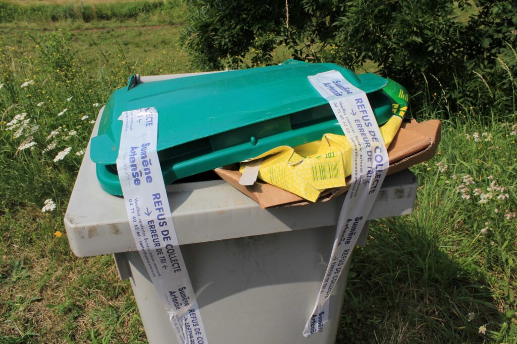 Poubelle d'un particulier avec du scotch scellant le couvercle avec la mention "Refus de collecte". Des cartons bruns dépassent du couvercle et sont la raison du refus de collecte de cette poubelle. - Agrandir l'image, fenêtre modale